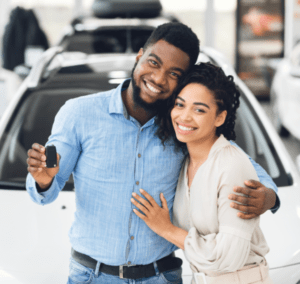 African American Couple Showing Car Key Standing In Automobile Dealership